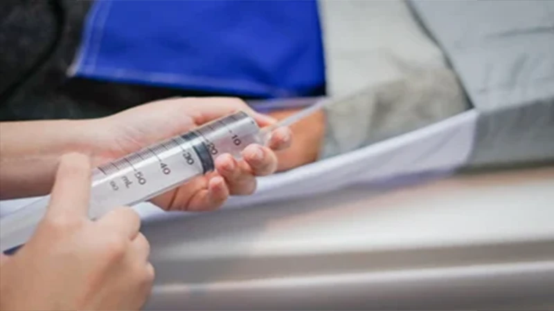 A clinical photo of a technologist administering IV contrast into a patient's arm before a scan.