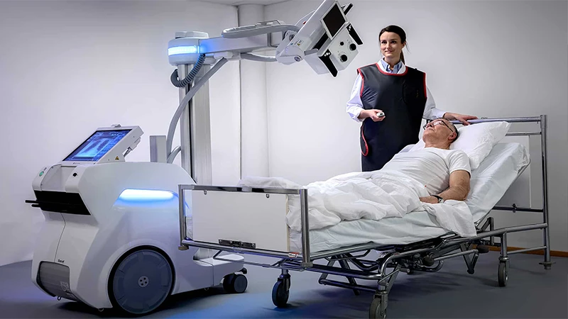 A technologist positioning a portable X-ray machine next to a patient's bed in an ICU.